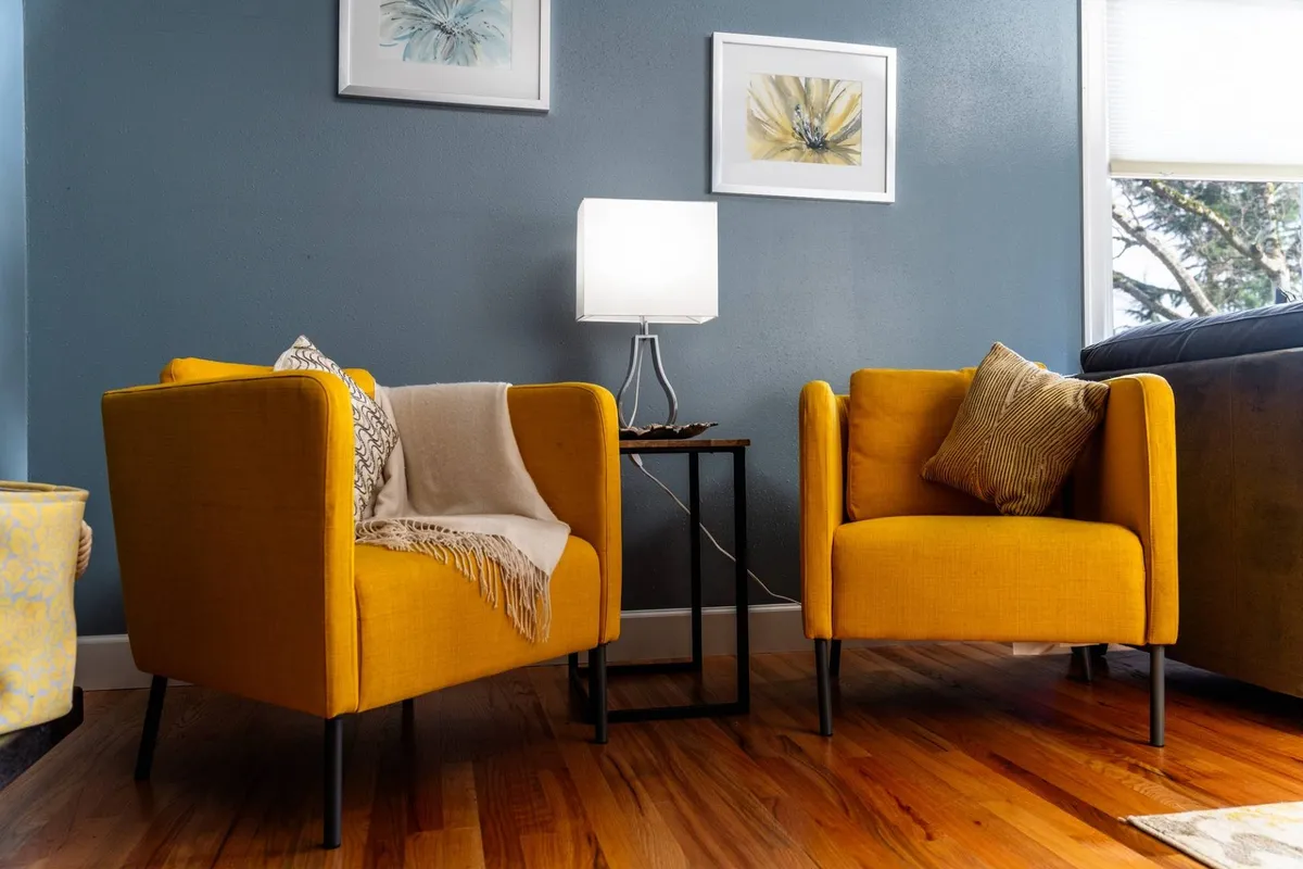 A cozy, light-filled sitting area features two cheerful yellow armchairs flanking a side table with a warm lamp, backed by tasteful artwork. This intimate corner is ideal for quiet conversation, reading, or simply unwinding, reinforcing the thoughtful, quiet ambiance described in the section.