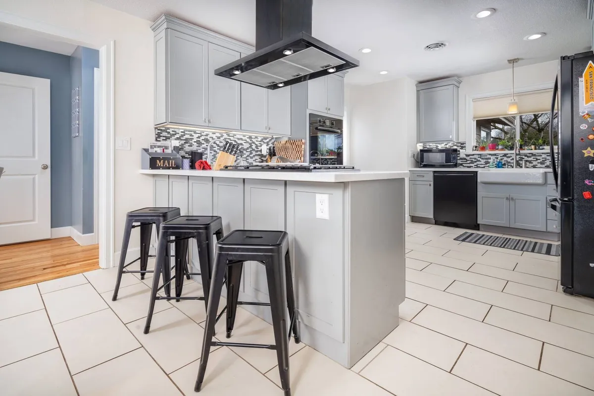 A modern kitchen centered around a functional island with stools, pristine appliances, and a stylish backsplash. The layout encourages both culinary creativity and casual interaction, suggesting ease of meal prep and informal gatherings around the island.