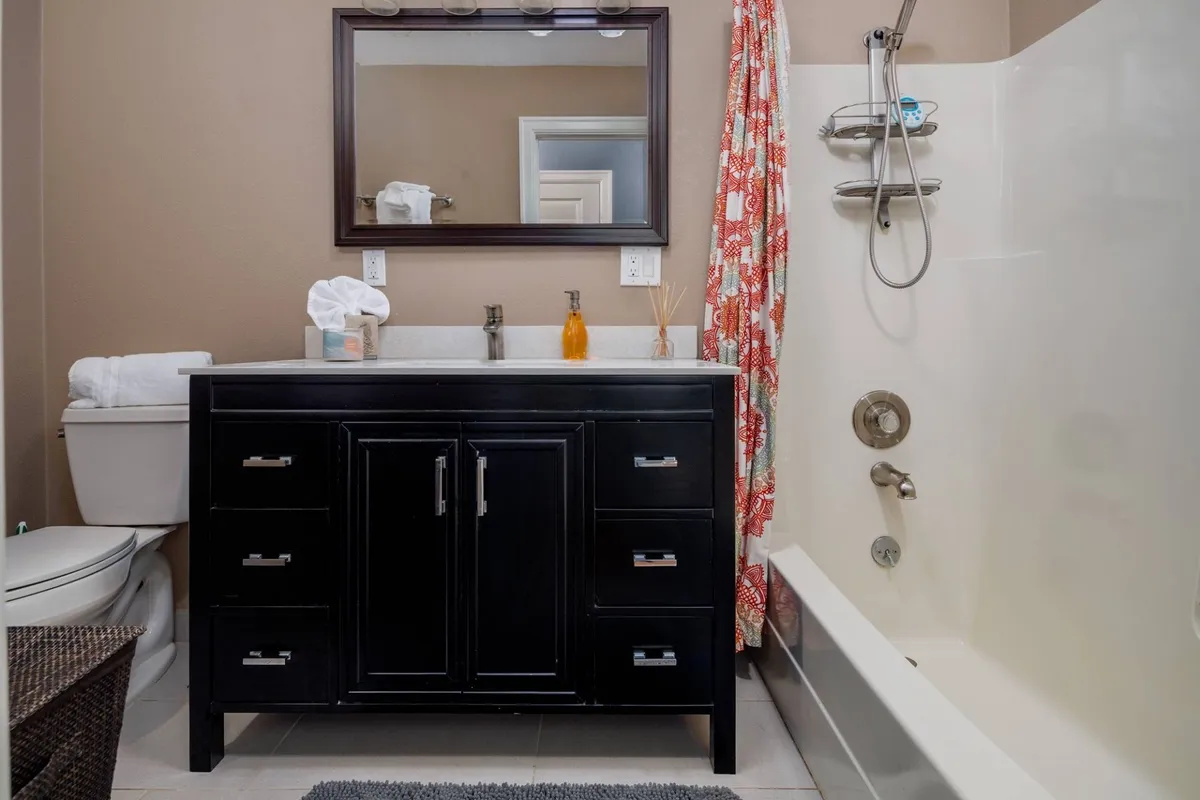 An inviting bathroom with a vanity, mirror, shower area, and a decorative curtain. The fresh and functional design provides an ideal setting for morning and evening routines.