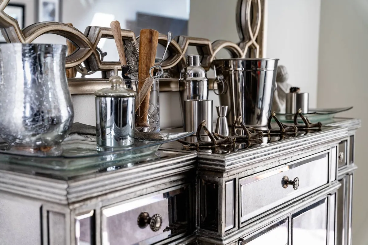 A stylish open-concept living and dining area, with barware, a decorative mirror, and textured surfaces. The space is set up for entertaining, with a chic yet comfortable ambiance perfect for gathering friends and hosting social events.