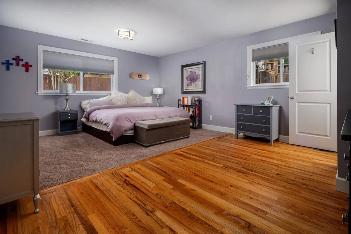 A peaceful bedroom scene featuring a neatly made bed flanked by matching nightstands, a piece of calming artwork above the headboard, and a window letting in soft natural light. The tranquil setting highlights comfortable linens and subtle décor touches that evoke a restful ambiance.